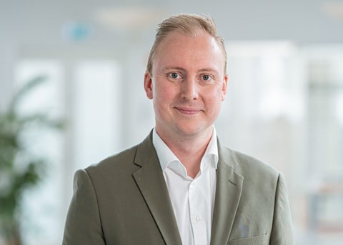 Jesper Andersen, Chief Financial Officer hos Conscensia, iført en grøn blazer og hvid skjorte, smilende i et kontormiljø.